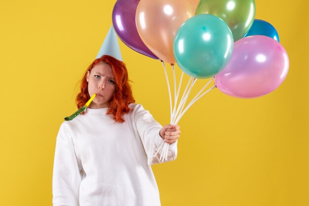 Vorderansicht der jungen Frau, die bunte Luftballons an der gelben Wand hält