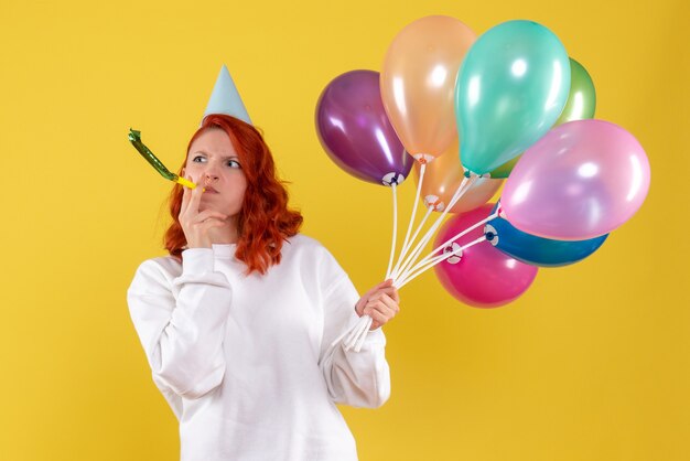 Vorderansicht der jungen Frau, die bunte Luftballons an der gelben Wand hält