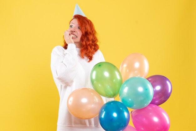 Vorderansicht der jungen Frau, die bunte Luftballons an der gelben Wand hält