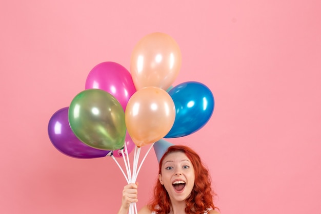 Vorderansicht der jungen Frau, die bunte Luftballons an der rosa Wand hält