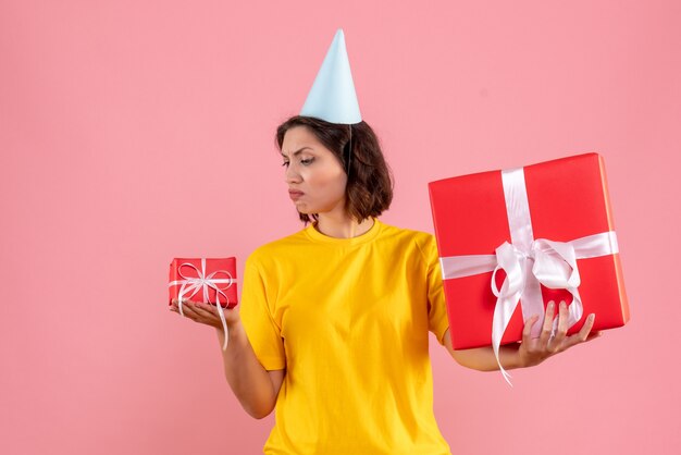 Vorderansicht der jungen Frau, die Geschenke an der rosa Wand hält