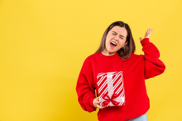 Vorderansicht der jungen Frau, die kleines Geschenk auf gelber Wand hält