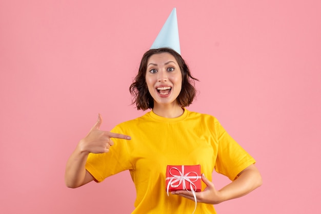 Vorderansicht der jungen Frau, die kleines Geschenk auf rosa Wand hält