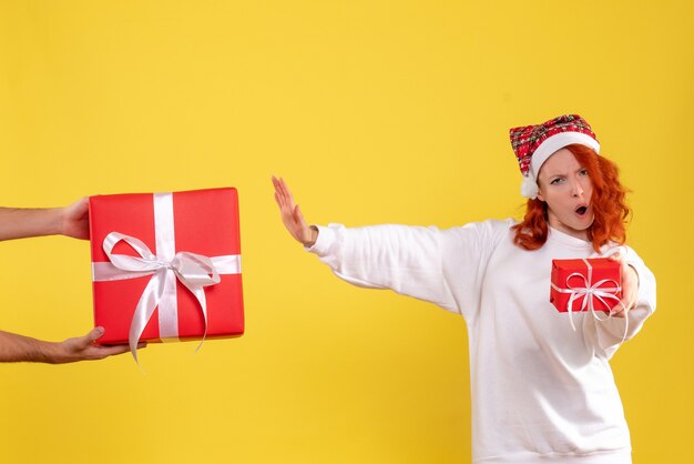 Vorderansicht der jungen Frau, die kleines Geschenk hält und großes auf gelber Wand ablehnt