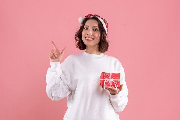 Vorderansicht der jungen Frau, die kleines Weihnachtsgeschenk an der rosa Wand hält