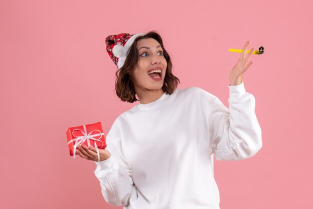 Vorderansicht der jungen Frau, die kleines Weihnachtsgeschenk an der rosa Wand hält