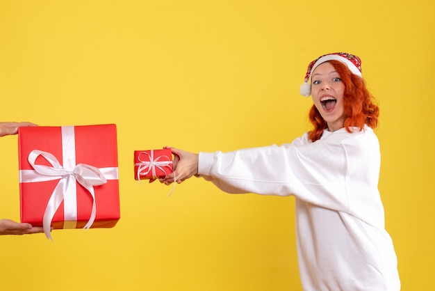 Vorderansicht der jungen Frau, die kleines Weihnachtsgeschenk auf gelber Wand hält