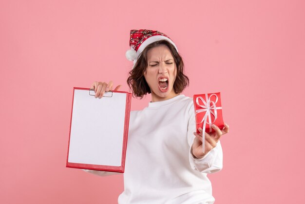 Vorderansicht der jungen Frau, die kleines Weihnachtsgeschenk und Aktennotiz auf der rosa Wand hält