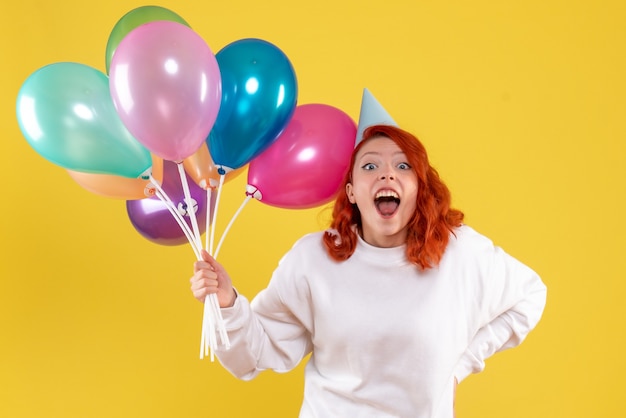 Vorderansicht der jungen Frau, die niedliche bunte Luftballons auf gelber Wand hält