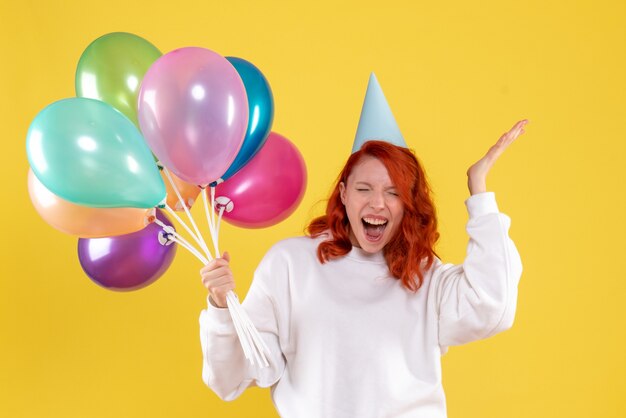 Vorderansicht der jungen Frau, die niedliche bunte Luftballons auf gelber Wand hält