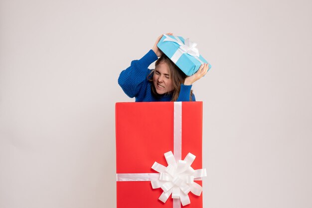 Vorderansicht der jungen Frau, die sich in der Geschenkbox an der weißen Wand versteckt