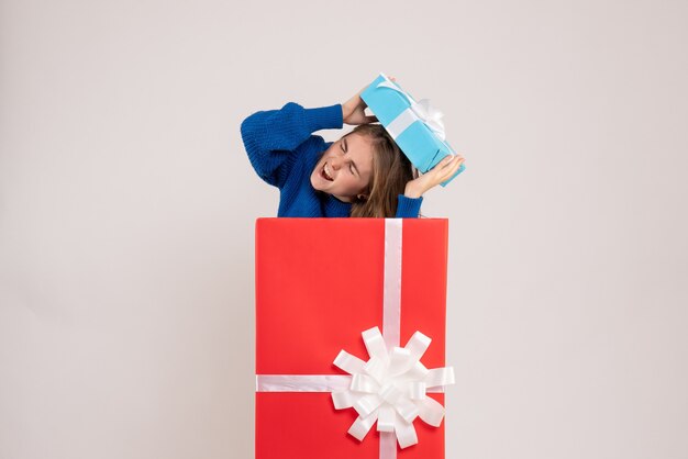 Vorderansicht der jungen Frau, die sich in der Geschenkbox an der weißen Wand versteckt