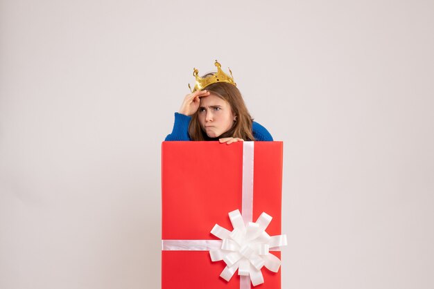 Vorderansicht der jungen Frau, die sich in der Geschenkbox an der weißen Wand versteckt