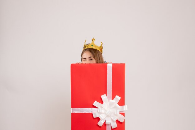 Vorderansicht der jungen Frau, die sich in der Geschenkbox an der weißen Wand versteckt