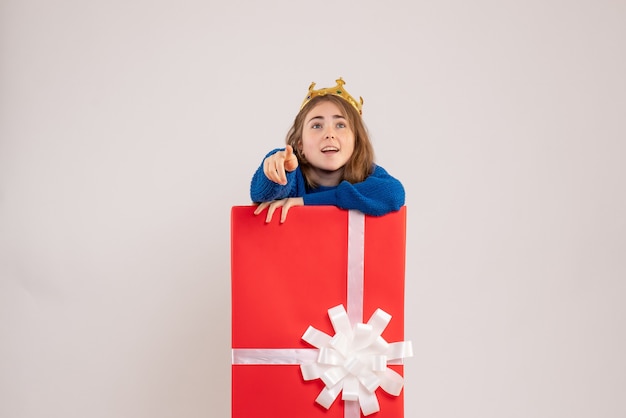 Vorderansicht der jungen Frau, die sich in der Geschenkbox an der weißen Wand versteckt