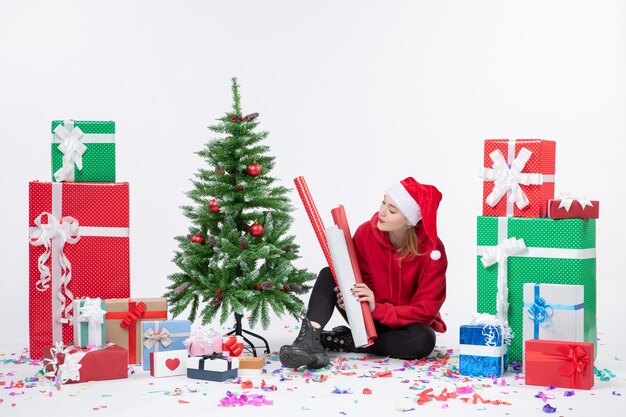 Vorderansicht der jungen Frau, die um Feiertagsgeschenke auf weißer Wand sitzt