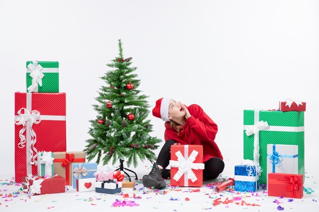 Vorderansicht der jungen Frau, die um Feiertagsgeschenke auf weißer Wand sitzt