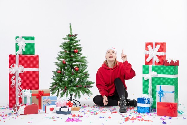 Vorderansicht der jungen Frau, die um Feiertagsgeschenke auf weißer Wand sitzt