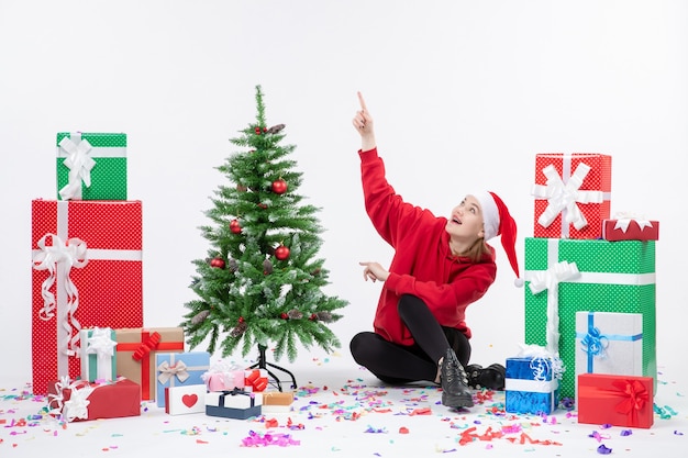 Vorderansicht der jungen Frau, die um Feiertagsgeschenke auf weißer Wand sitzt