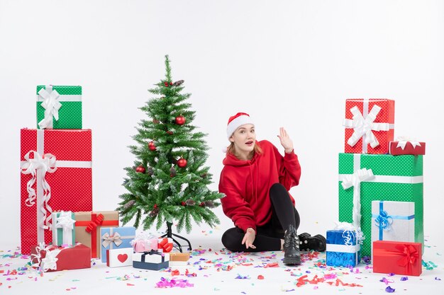 Vorderansicht der jungen Frau, die um Feiertagsgeschenke auf weißer Wand sitzt