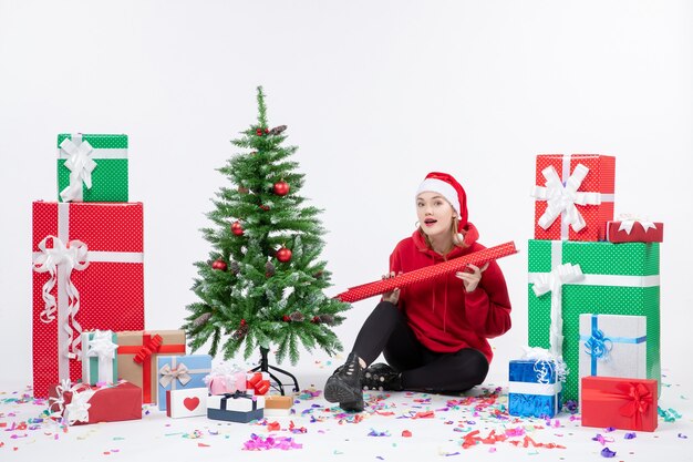 Vorderansicht der jungen Frau, die um Feiertagsgeschenke auf weißer Wand sitzt