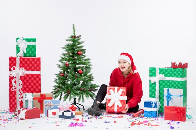 Vorderansicht der jungen Frau, die um Feiertagsgeschenke auf weißer Wand sitzt