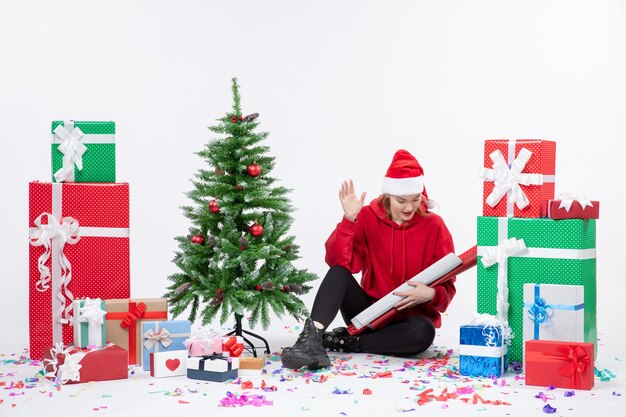 Vorderansicht der jungen Frau, die um Feiertagsgeschenke auf weißer Wand sitzt