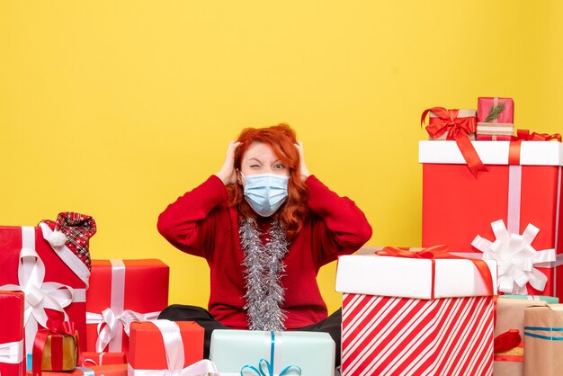 Vorderansicht der jungen Frau, die um Geschenke in der Maske auf gelber Wand sitzt