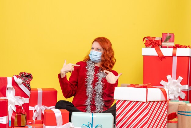 Vorderansicht der jungen Frau, die um Geschenke in der Maske sitzt, die auf gelber Wand missfiel