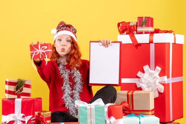 Vorderansicht der jungen Frau, die um Weihnachten sitzt, präsentiert mit Aktennotiz auf gelber Wand