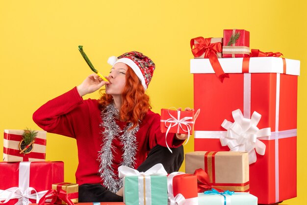 Vorderansicht der jungen Frau, die um Weihnachtsgeschenke auf gelber Wand sitzt