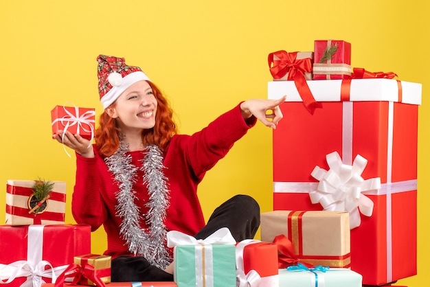 Vorderansicht der jungen Frau, die um Weihnachtsgeschenke auf gelber Wand sitzt