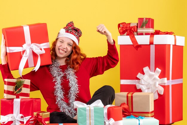 Vorderansicht der jungen Frau, die um Weihnachtsgeschenke auf gelber Wand sitzt