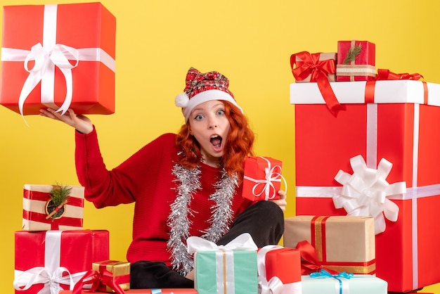 Vorderansicht der jungen Frau, die um Weihnachtsgeschenke auf gelber Wand sitzt