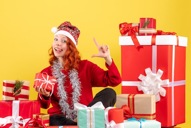 Vorderansicht der jungen Frau, die um Weihnachtsgeschenke auf gelber Wand sitzt