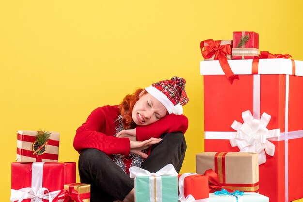 Vorderansicht der jungen Frau, die um Weihnachtsgeschenke auf gelber Wand sitzt