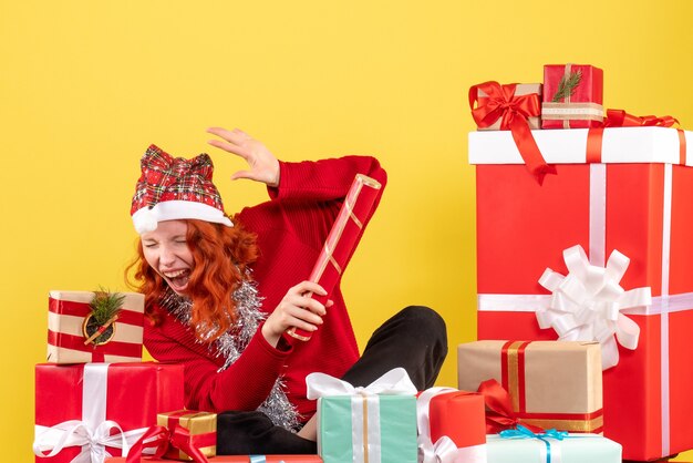 Vorderansicht der jungen Frau, die um Weihnachtsgeschenke auf gelber Wand sitzt