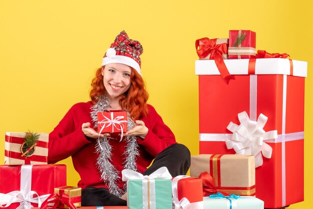 Vorderansicht der jungen Frau, die um Weihnachtsgeschenke auf gelber Wand sitzt