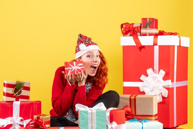 Vorderansicht der jungen Frau, die um Weihnachtsgeschenke auf gelber Wand sitzt