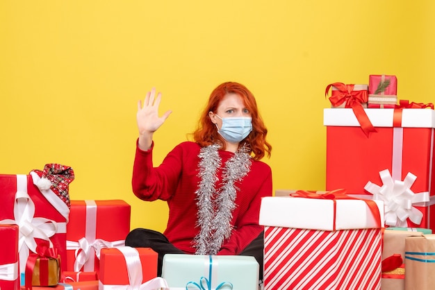 Vorderansicht der jungen Frau, die um Weihnachtsgeschenke in der Maske auf gelber Wand sitzt