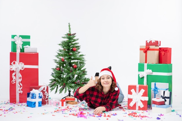 Vorderansicht der jungen Frau, die um Weihnachtsgeschenke und kleinen Feiertagsbaum auf weißer Wand legt