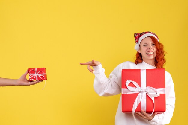 Vorderansicht der jungen Frau, die Weihnachten Geschenk auf gelber Wand hält