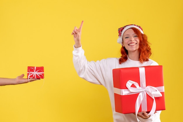 Vorderansicht der jungen Frau, die Weihnachten Geschenk auf gelber Wand hält