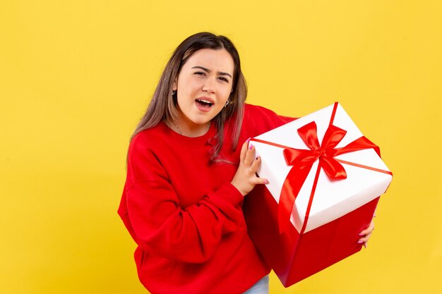 Vorderansicht der jungen Frau, die Weihnachtsgeschenk auf gelber Wand hält