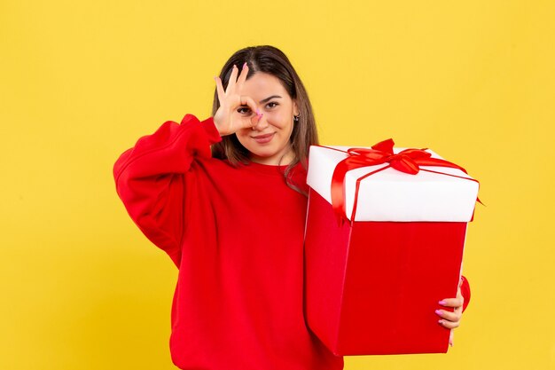 Vorderansicht der jungen Frau, die Weihnachtsgeschenk auf gelber Wand hält