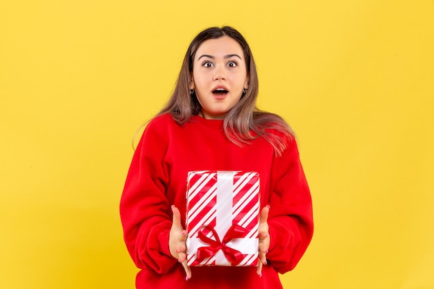 Vorderansicht der jungen frau, die weihnachtsgeschenk auf gelber wand hält