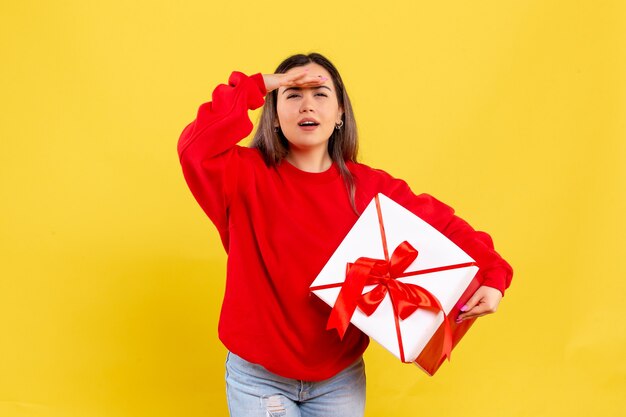 Vorderansicht der jungen Frau, die Weihnachtsgeschenk auf gelber Wand hält