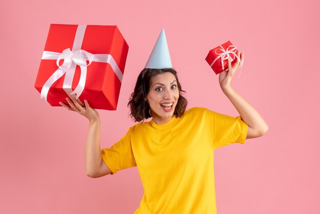 Vorderansicht der jungen Frau, die Weihnachtsgeschenke an der rosa Wand hält