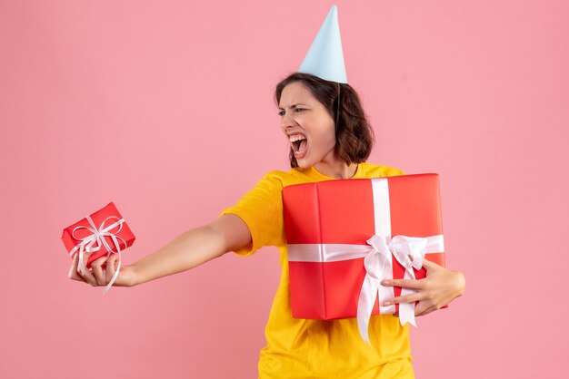 Vorderansicht der jungen Frau, die Weihnachtsgeschenke an der rosa Wand hält