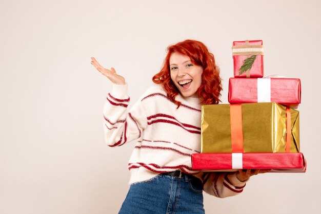 Vorderansicht der jungen Frau, die Weihnachtsgeschenke auf weißer Wand trägt